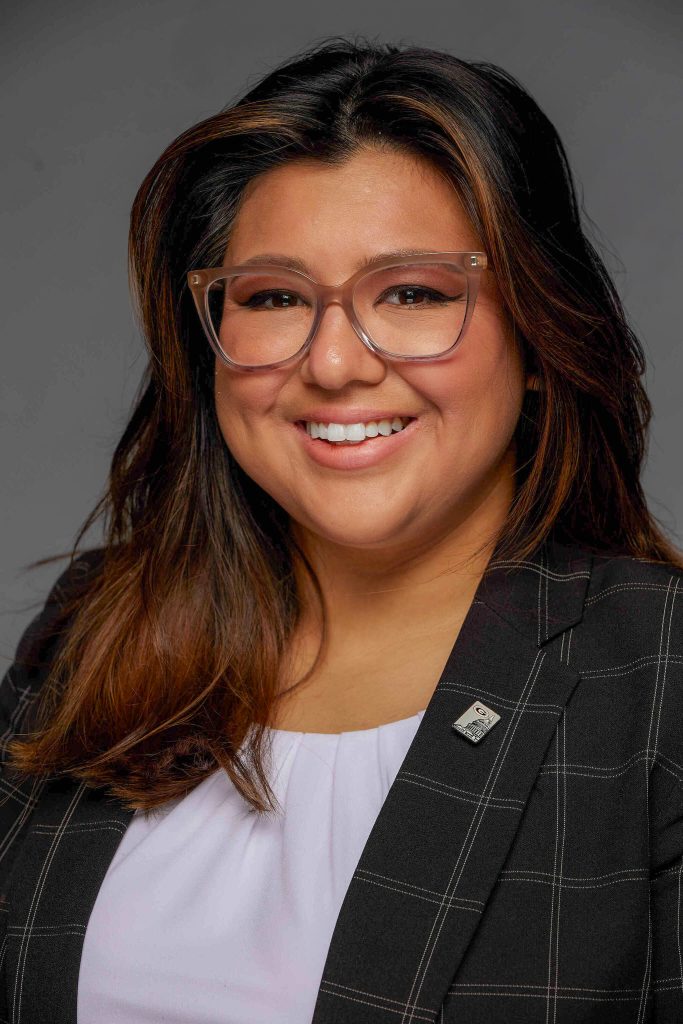 Woman in glasses and blazer smiling.